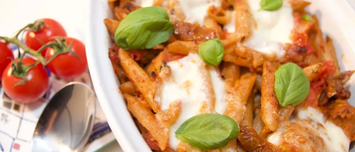 Cheesy pasta dish with vegetarian sausages and topped with mozzarella cheese and basil
